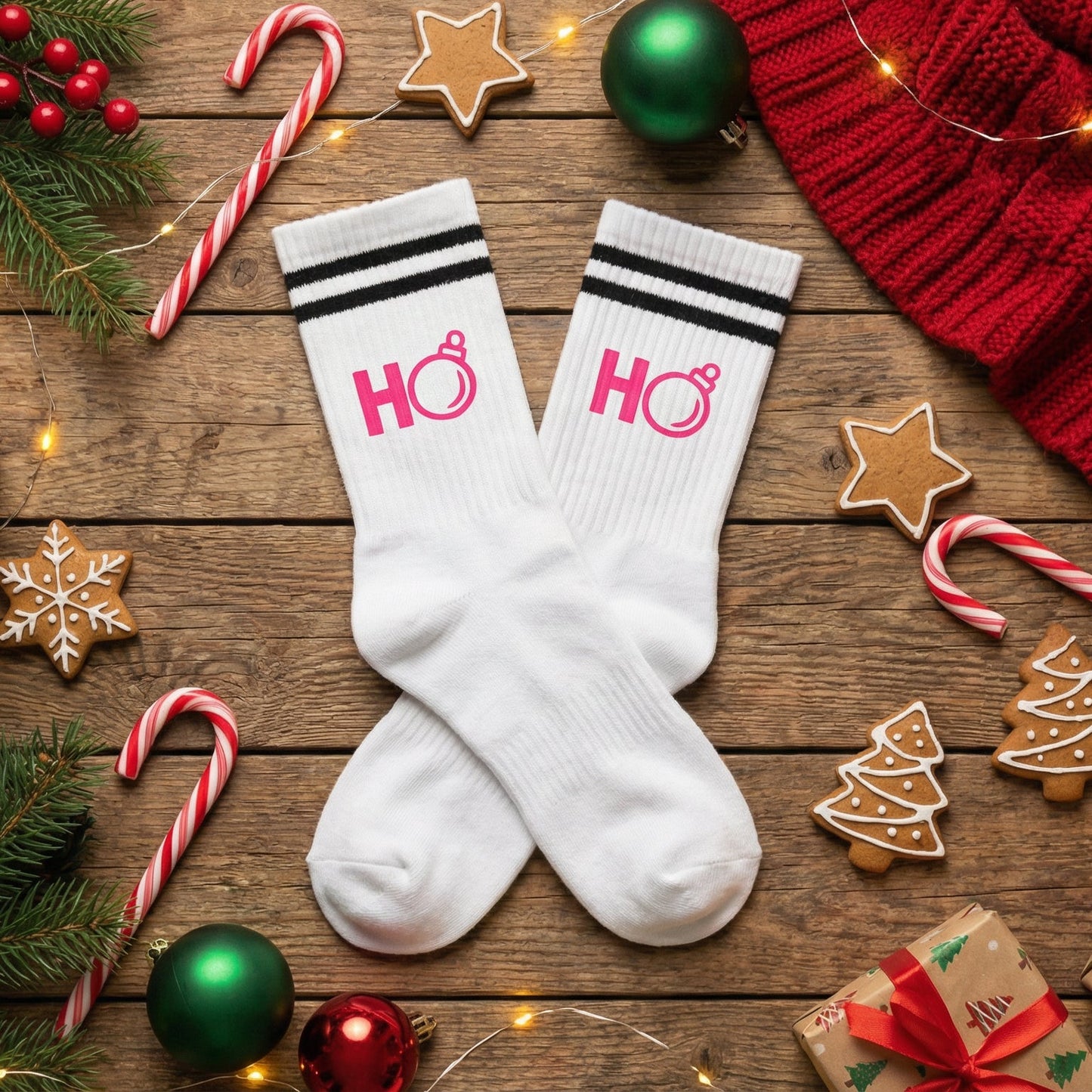 Weiße TinyTypo Socke mit pinkem „Ho Ho“ Print und Partyhut-Icon, dekoriert zwischen Weihnachtskugeln, Tannenzweigen, Geschenken und Kakao.
