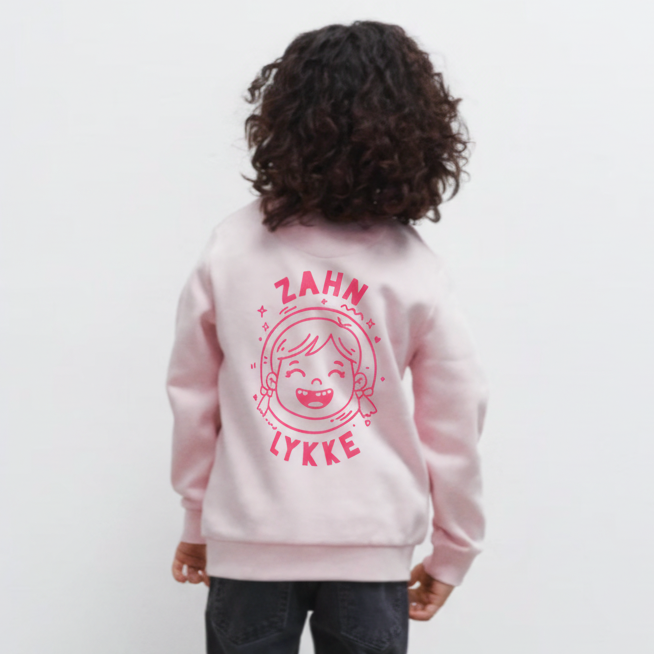 Kind von hinten in soft pink „Zahn Lykke“ Kinder-Sweatshirt, dunkle Jeans und weißen Sneakern.