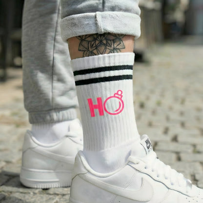 Weiße Socke mit pinkem „Ho“ Weihnachtsmotiv, getragen zu weißen Sneakern; urbaner Look auf Kopfsteinpflaster.