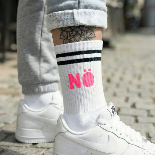 Weiße Socke mit pinkem „NÖ“ Statement-Print, getragen zu weißen Sneakern im Streetstyle auf Kopfsteinpflaster.