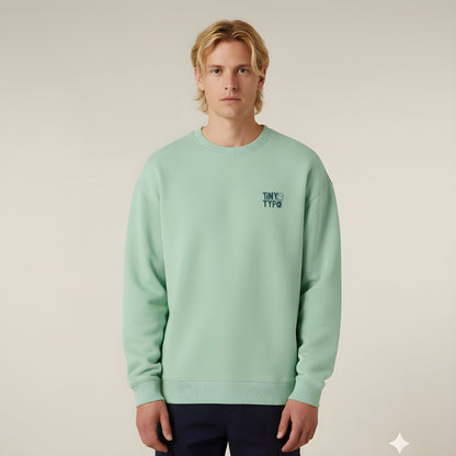 Jade grüner Unisex Sweater von Tiny Typo – Vorderseite mit kleinem Logo-Print, Rückseite mit HoHoHoppla Weihnachtsmotiv.